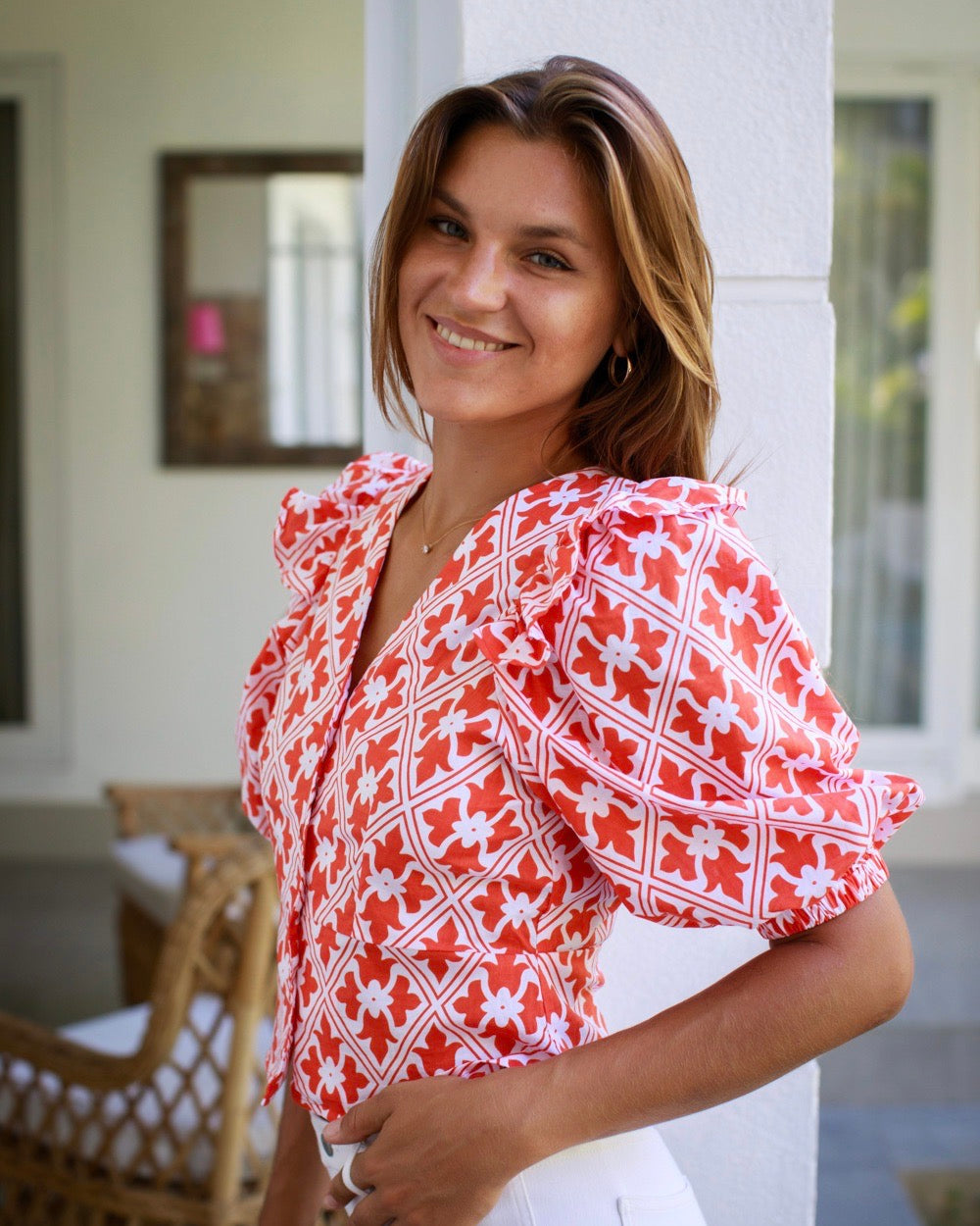 A woman smiling and posing in an orange and white geometric patterned top with short puffed sleeves and a round neckline.