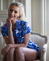 Woman in bedroom in blue leaf printed pjs with shirt style top and matching short bottoms.