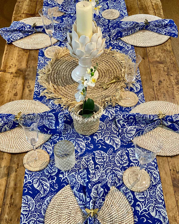 Table setting featuring white rattan placemats and blue/white leaf table runner.