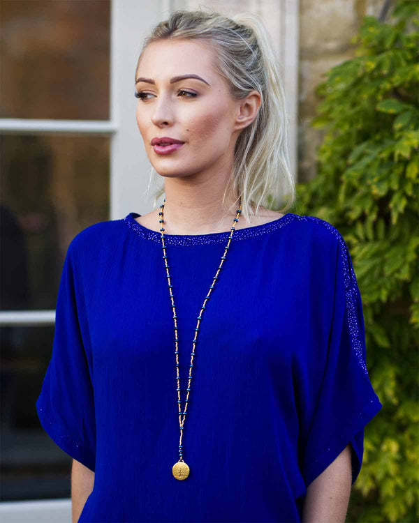 Woman in cobalt blue top, outisde, wearing a cobalt crystal necklace with a tree of life pendant.